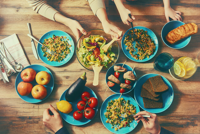 hands reach for bowls around a table filled with food